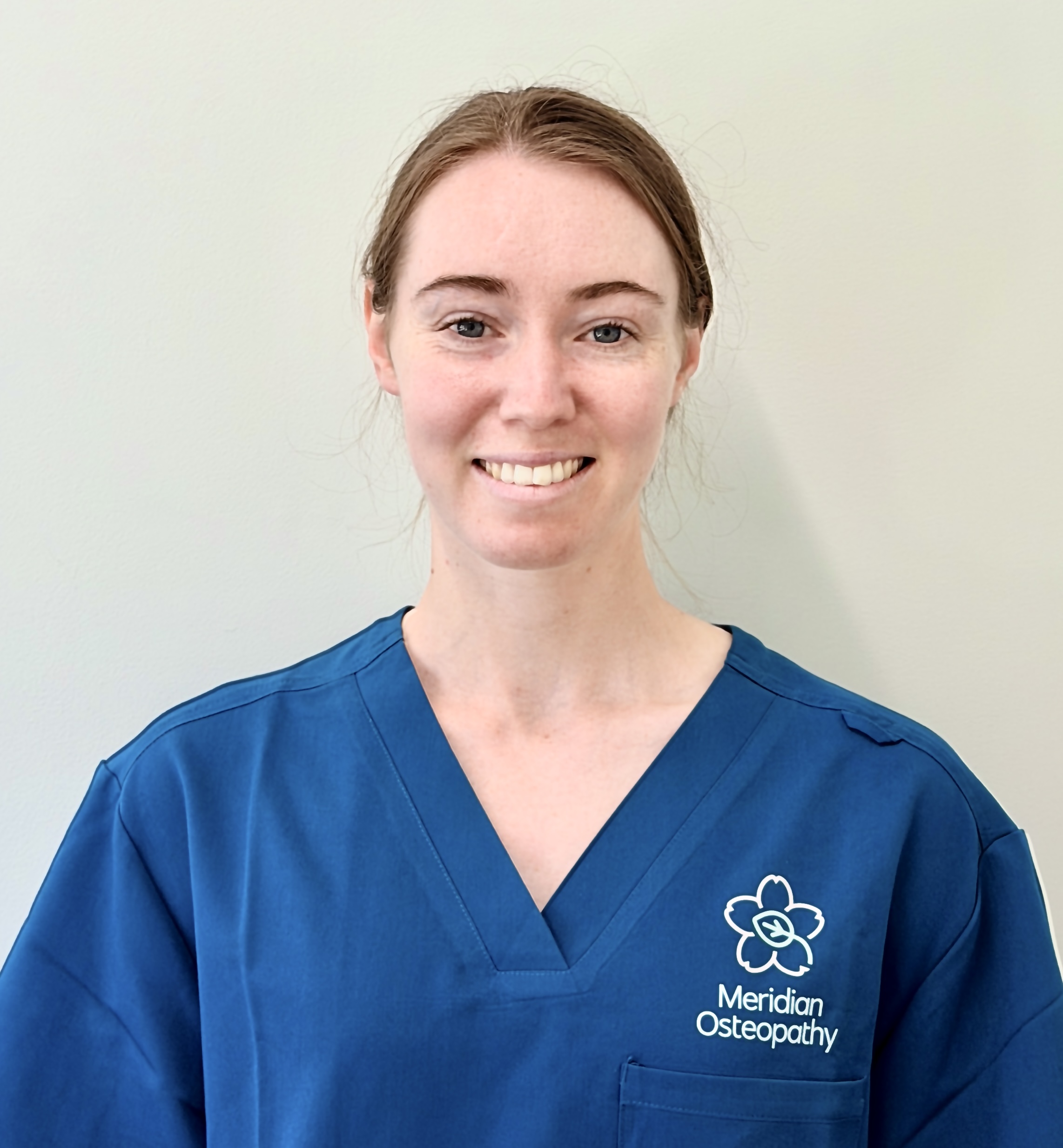 Osteopath Kaylee Frost of Meridian Osteopathy, smiling in branded teal clinical scrubs